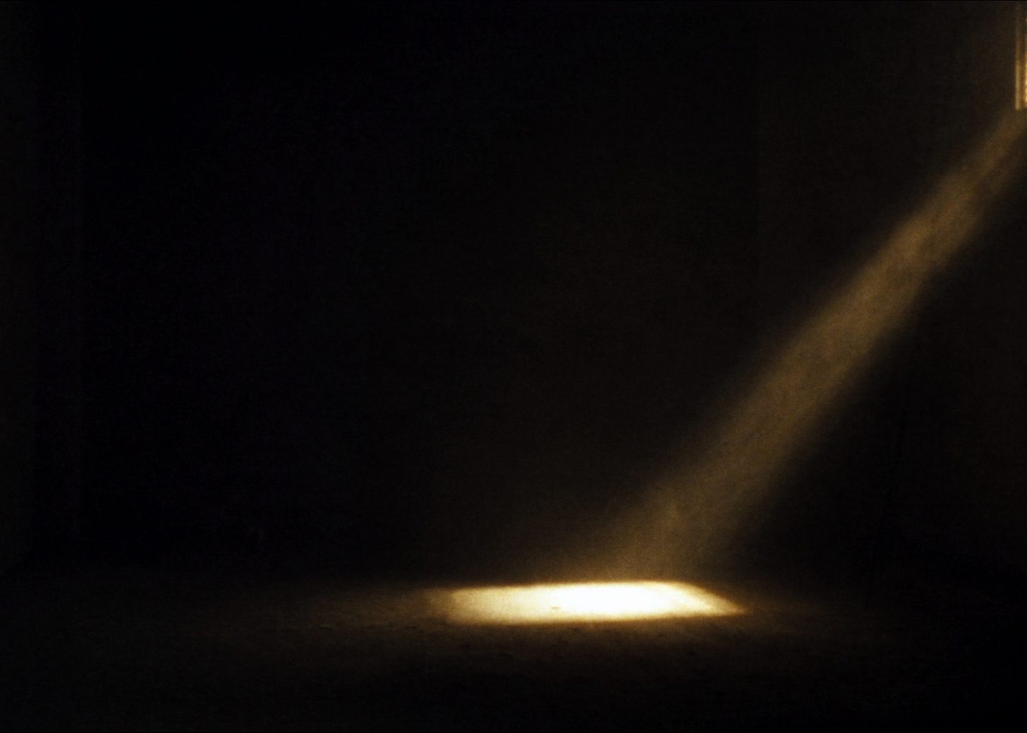 Facho de luz entrando por uma janela alta e pousando no chão de uma sala escura